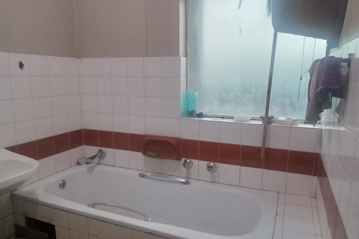 A dated bathroom featuring a built-in bathtub with white and terracotta wall tiling and a frosted glass window.