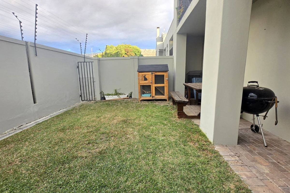 A private rear garden featuring a paved patio area, a small lawn, and perimeter boundary walls with security fencing.