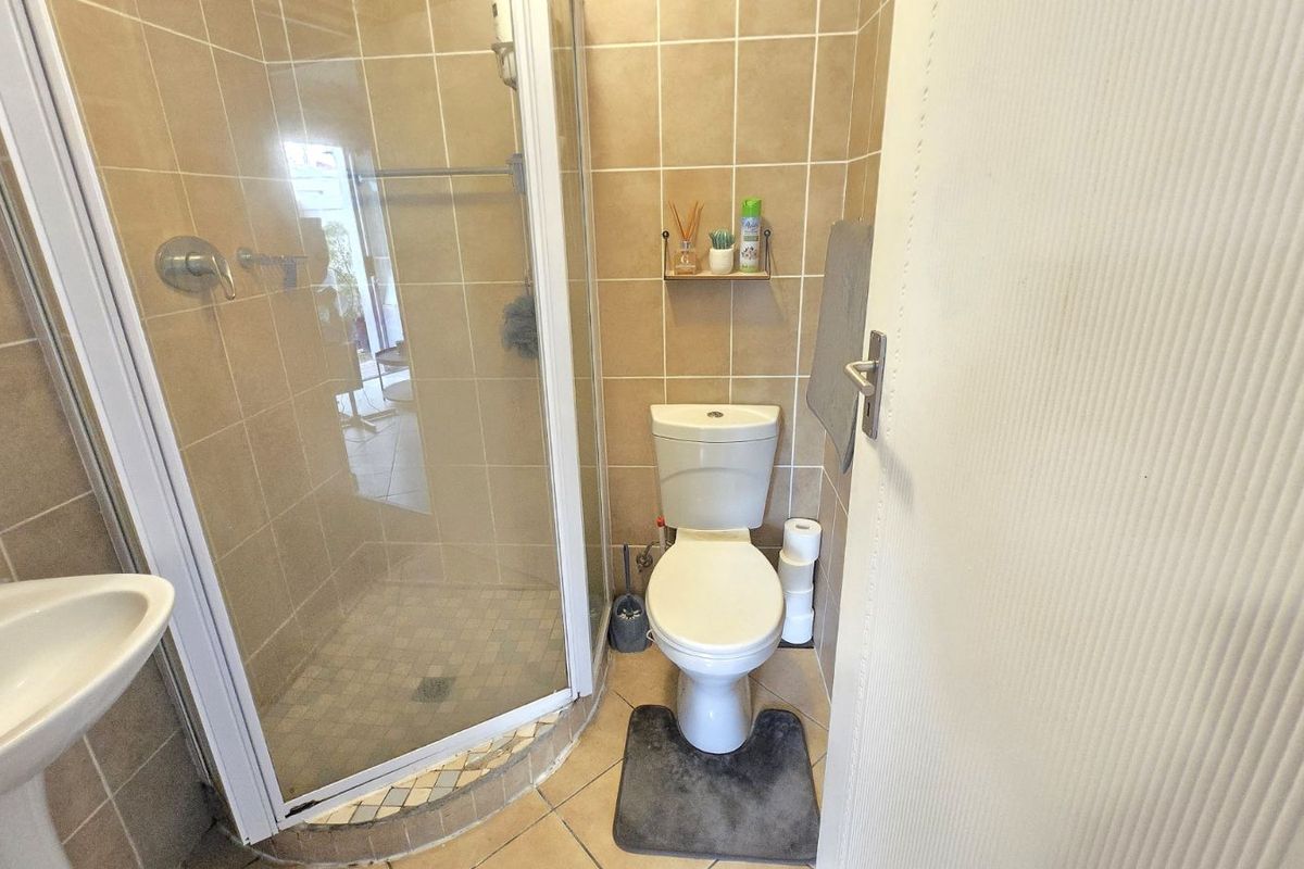 Compact bathroom featuring a corner glass shower enclosure, pedestal basin, and toilet with neutral wall tiling.