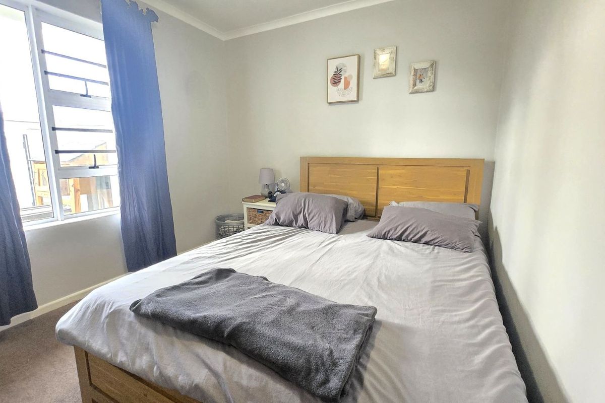 A well-lit bedroom featuring neutral wall finishes, carpeted flooring, and a large window providing natural light.