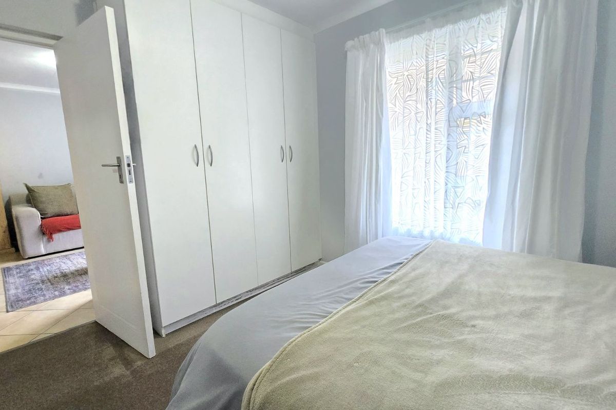 A bright bedroom featuring built-in floor-to-ceiling wardrobes and carpeted flooring, with a view into the adjacent living area.