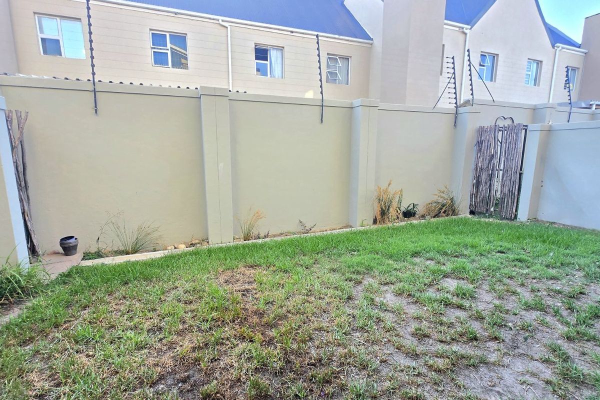 A private rear garden area featuring a lawn and high boundary walls with integrated electric fencing for added security.