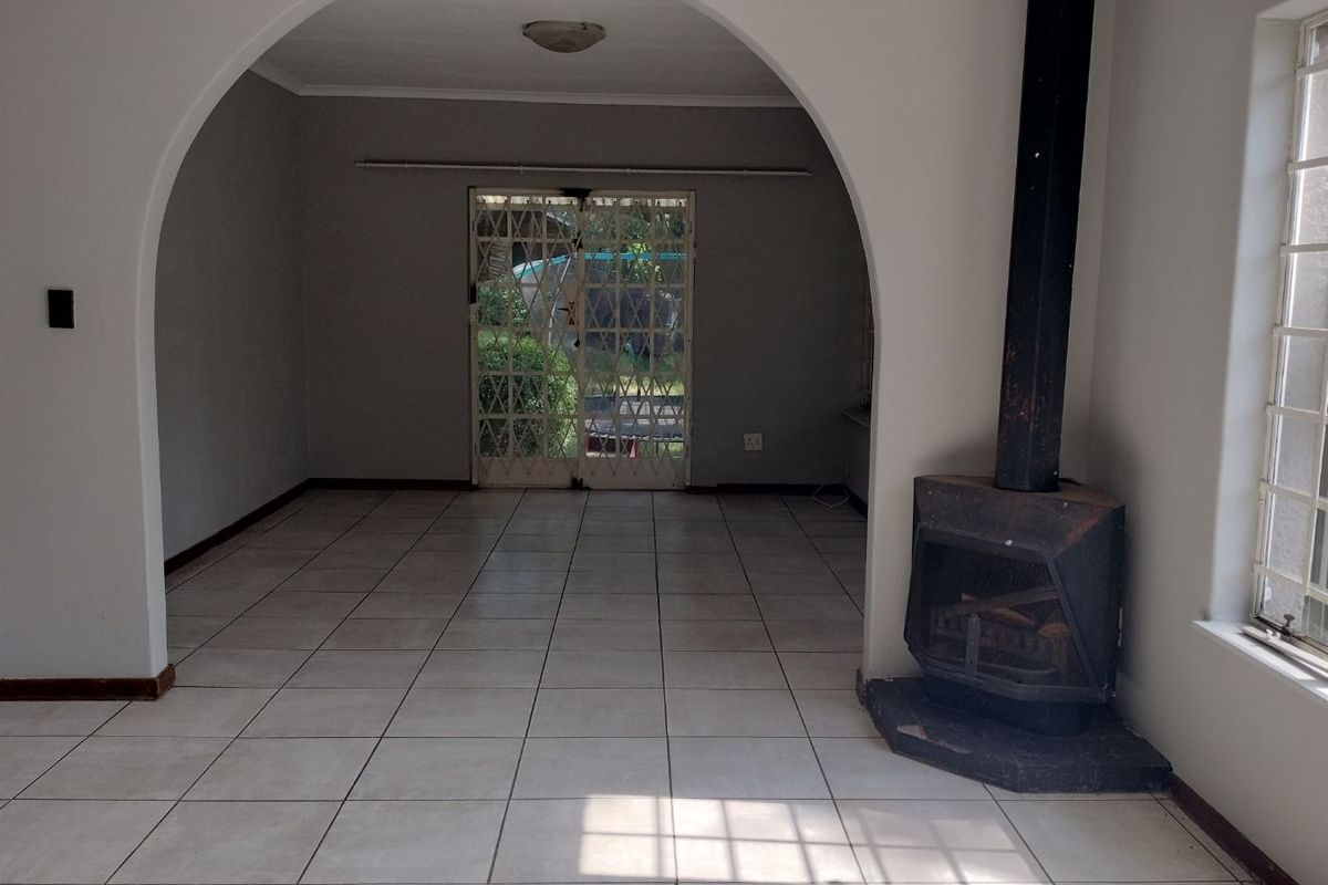 Spacious living area featuring tiled flooring, a prominent arched entryway, and a built-in fireplace, leading out to the rear garden through security gates.