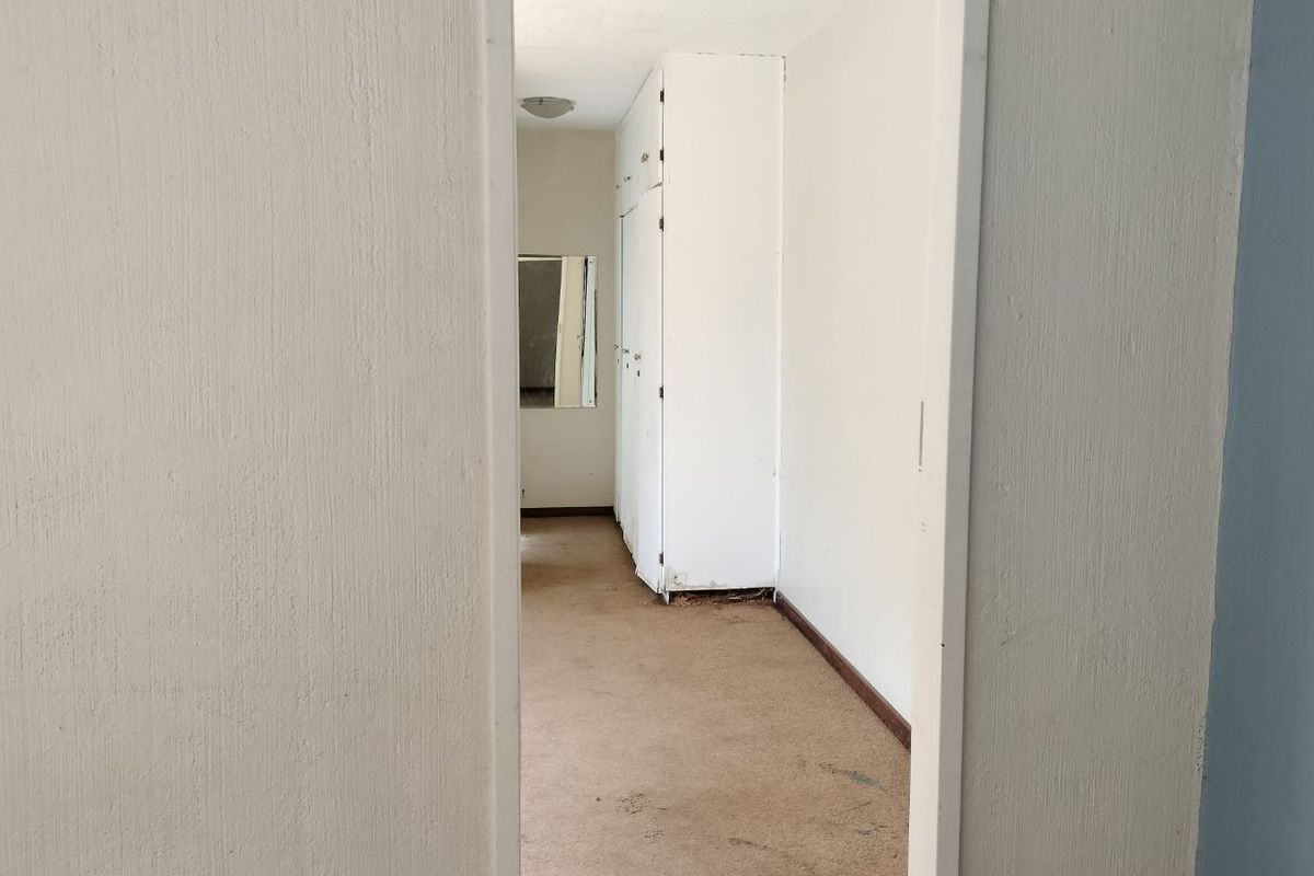 A view into a bedroom featuring built-in cupboards and carpeted flooring, showing signs of wear and requiring cosmetic updates.