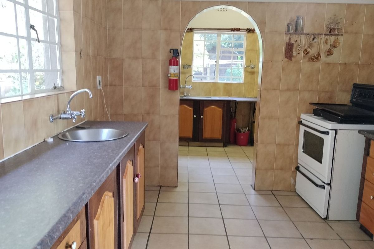 Kitchen featuring tiled walls, built-in cabinetry, a stainless steel sink, and a freestanding stove, with an adjoining scullery area visible through the archway.