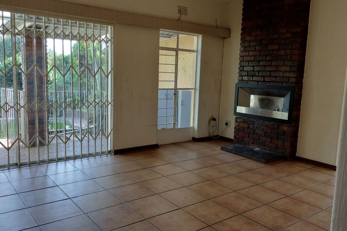 Spacious living room featuring a built-in brick fireplace, tiled flooring, and sliding security gates providing access to the outdoor patio area.