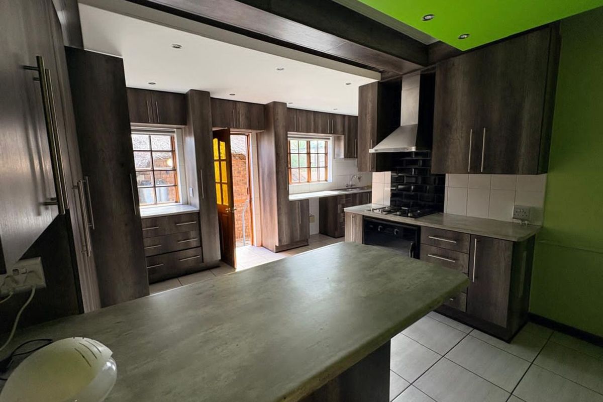 Spacious kitchen featuring dark wood-look cabinetry, stone-style countertops, built-in oven, extractor fan, and tiled flooring with direct access to the exterior.