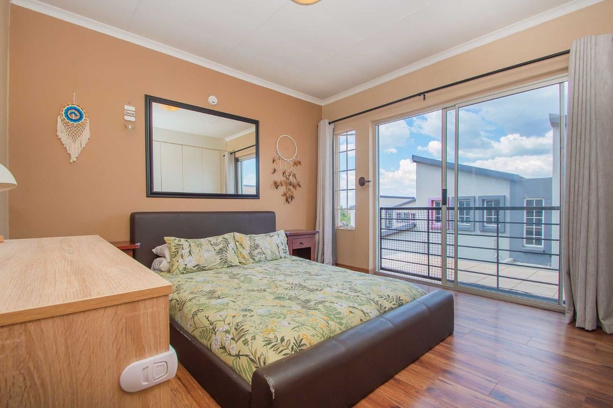 A well-lit bedroom featuring laminate flooring, a large sliding glass door leading to a balcony, and neutral wall finishes.