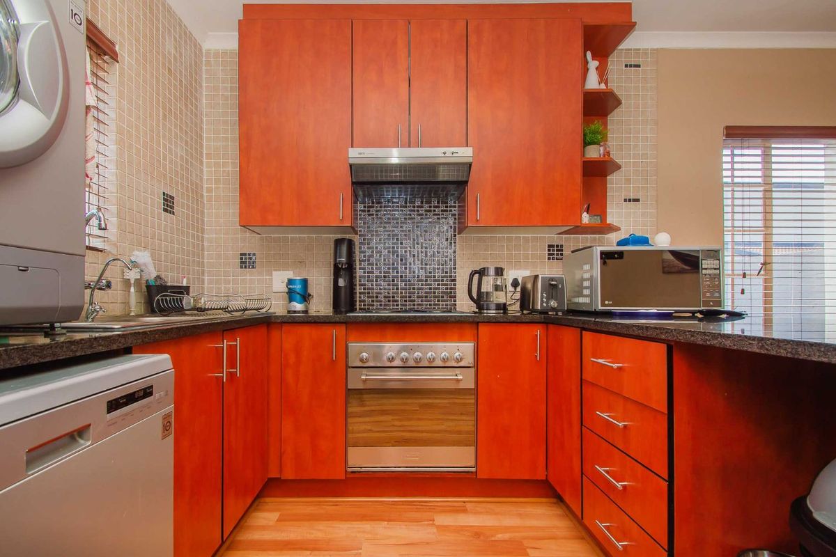 A functional kitchen featuring cherry-wood cabinetry, granite countertops, a built-in oven with extractor fan, and mosaic tile splashbacks.