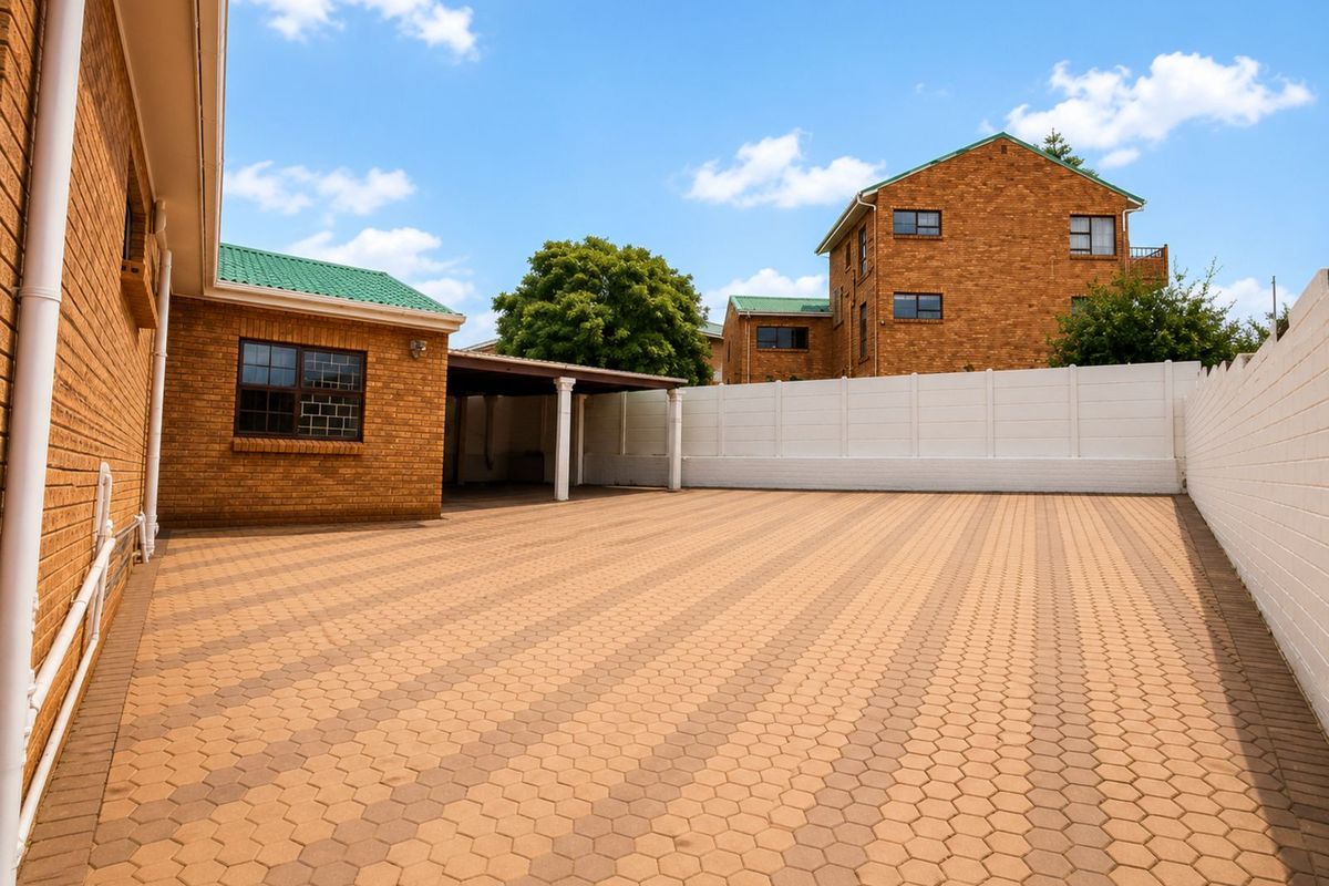 Spacious paved rear courtyard area featuring a covered carport and perimeter boundary walls, providing ample outdoor space and parking potential.