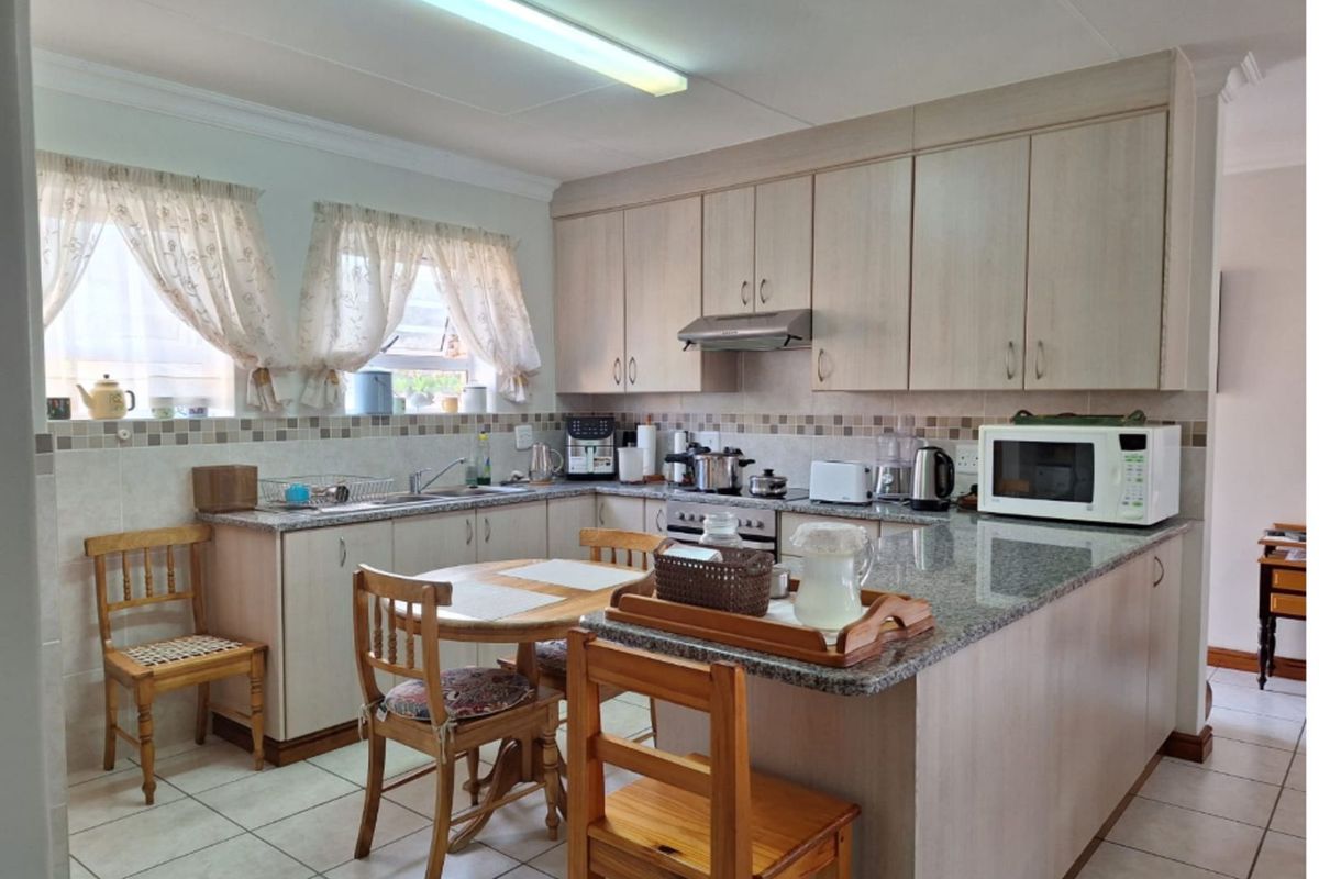 A functional kitchen featuring light wood cabinetry, granite countertops, tiled flooring, and a built-in extractor fan with a breakfast nook area.