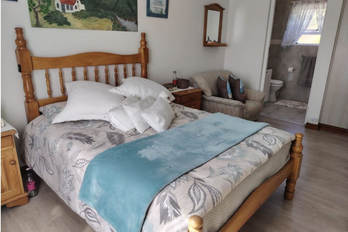 A well-maintained bedroom featuring light-toned laminate flooring and an en-suite bathroom with tiled finishes.