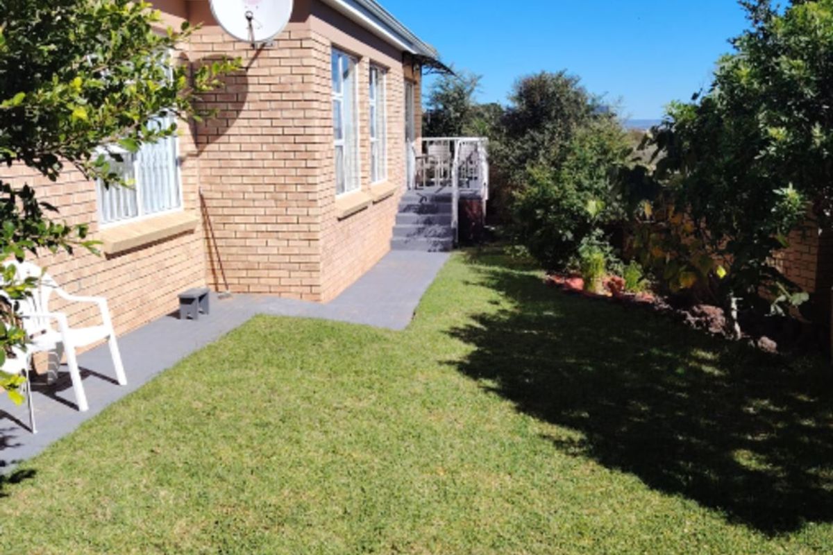 A view of the rear garden and exterior brick facade, featuring a paved walkway and access to a raised patio area.
