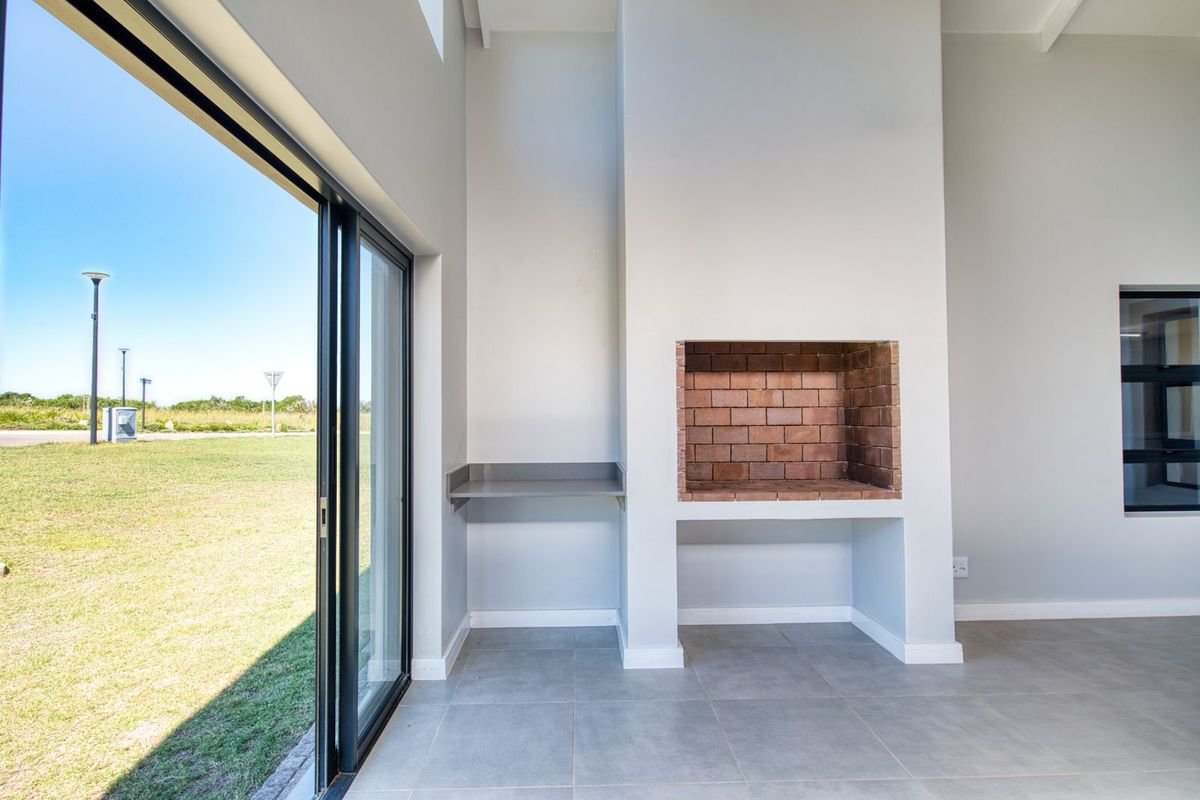 A bright, modern living area featuring a built-in brick fireplace, tiled flooring, and large sliding glass doors opening to the garden.