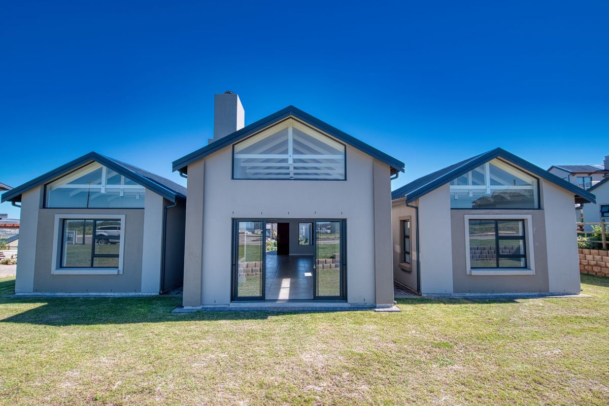 A modern rear elevation of a house featuring large glass windows, sliding doors, and a clean, contemporary architectural design with a well-maintained lawn.