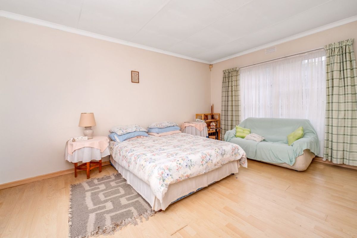 A spacious bedroom featuring light-toned laminate flooring, neutral walls, and large windows with curtains, offering a comfortable and functional living space.