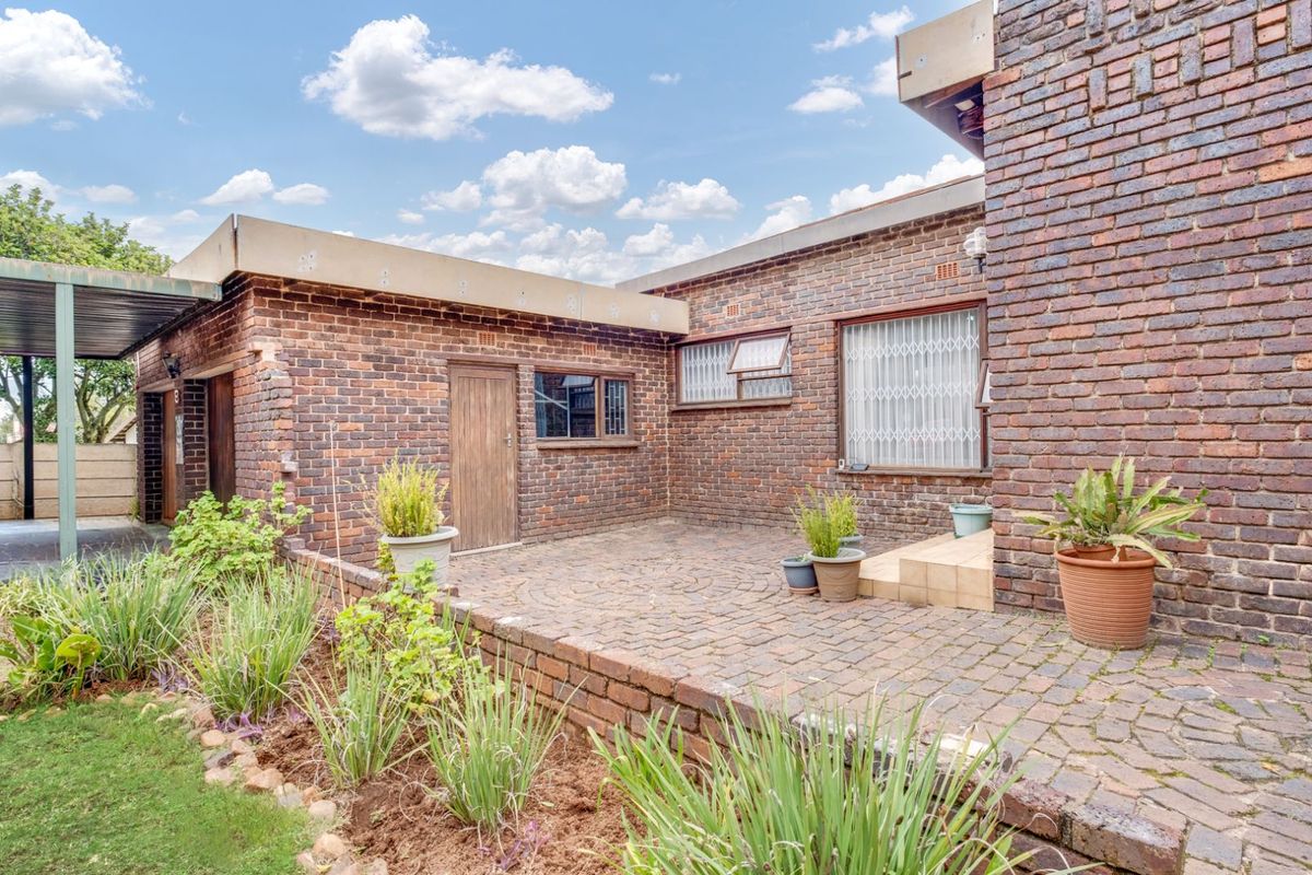 A private rear courtyard featuring brick paving, established garden beds, and direct access to the main dwelling structure.