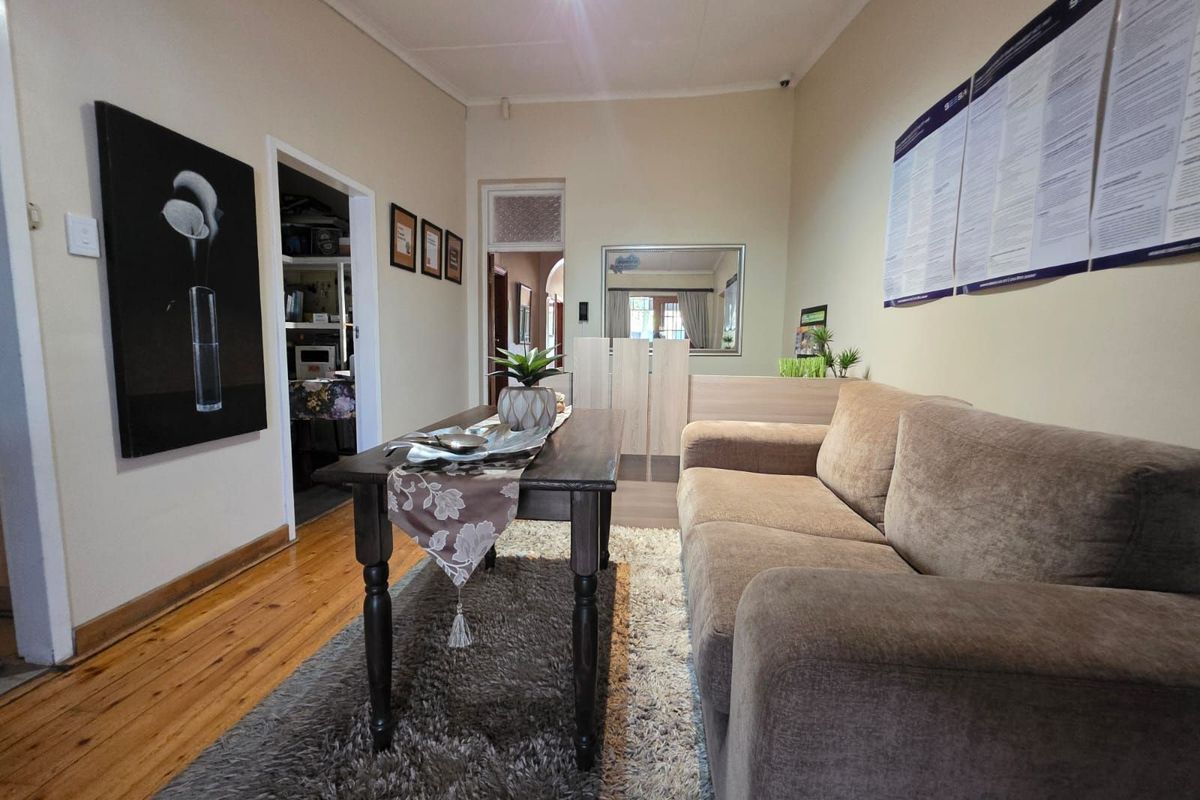A functional living area featuring polished wooden flooring, neutral wall tones, and access to adjacent rooms within the guest house.
