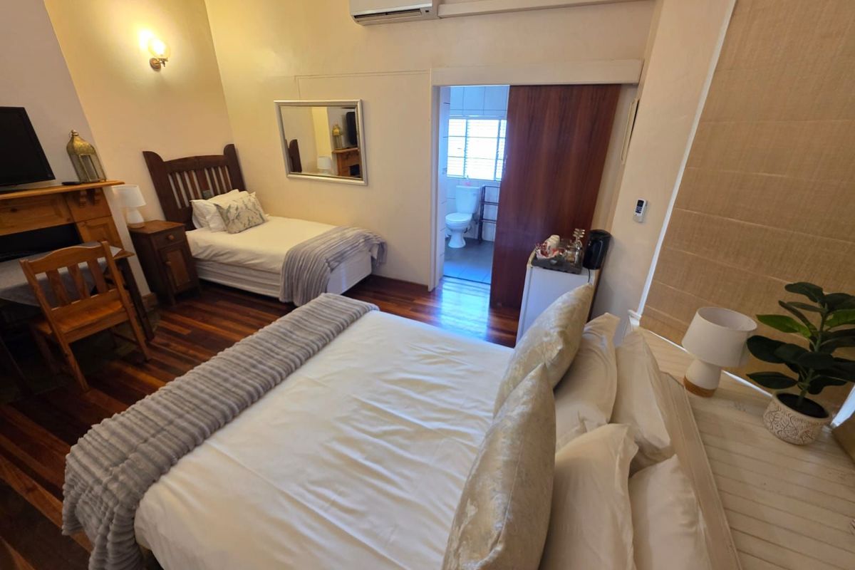 A guest bedroom featuring hardwood flooring, a wall-mounted air conditioning unit, and an en-suite bathroom accessible through a sliding door.