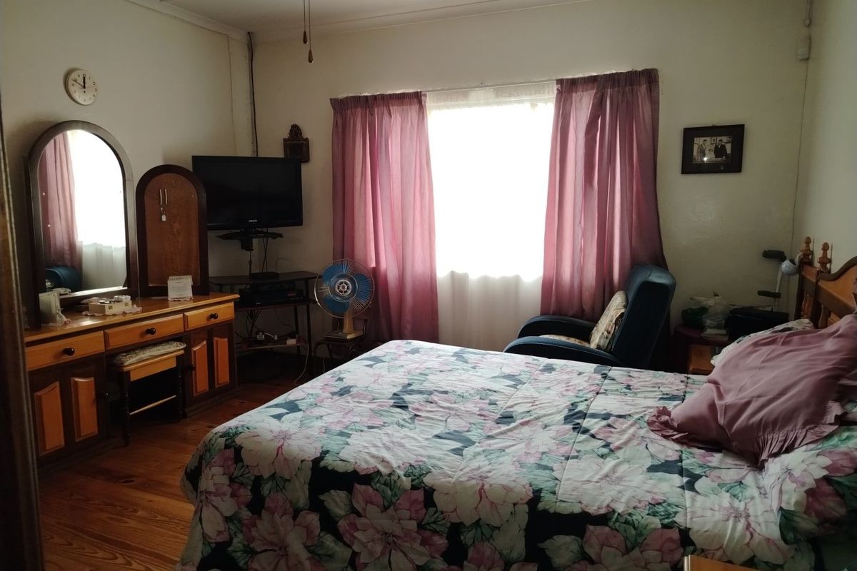 A functional bedroom featuring timber flooring and a large window with curtains, providing a comfortable and lived-in space.