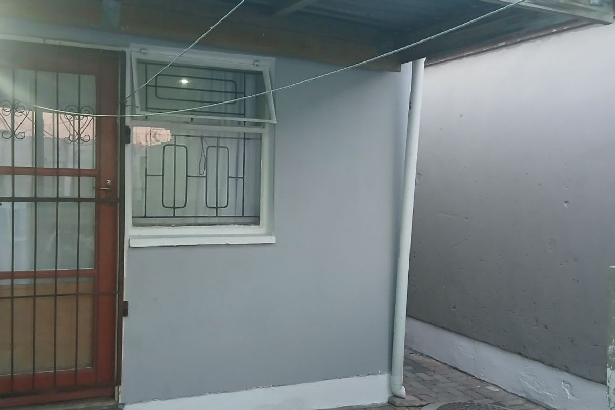 Exterior view of a side entrance featuring a security gate, window with burglar bars, and a covered walkway area.