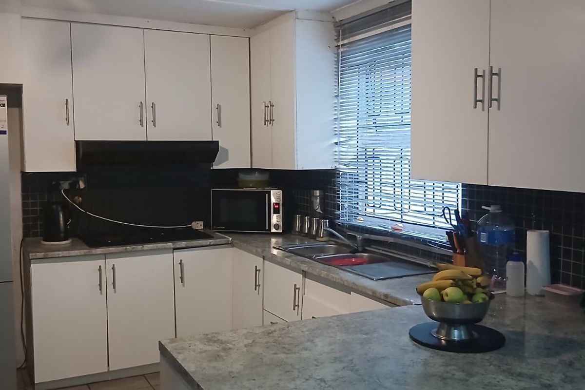 A functional kitchen featuring white cabinetry, dark tiled splashbacks, stone-look laminate countertops, and a double stainless steel sink.