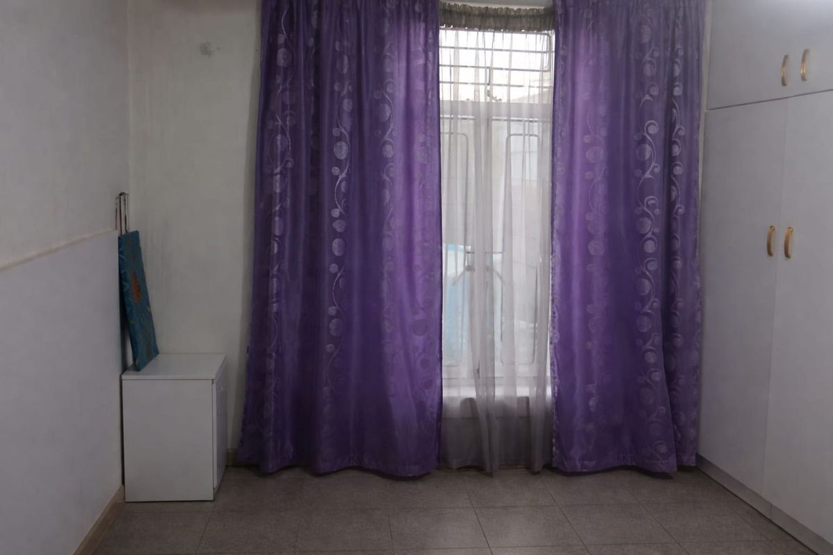 A bedroom featuring built-in white cabinetry and a window with security bars, finished with tiled flooring.