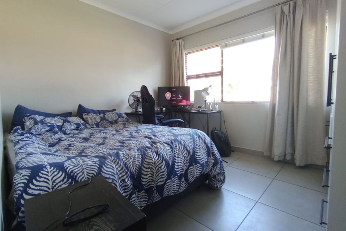 A functional bedroom featuring large format floor tiles, neutral wall finishes, and a window with curtain tracks.