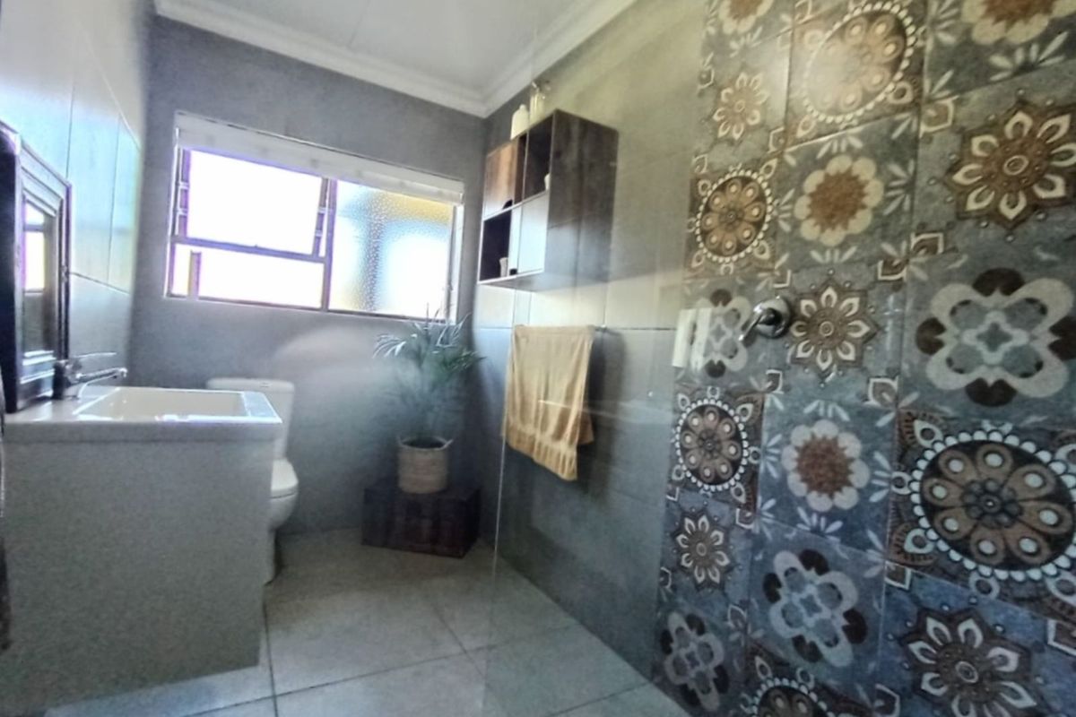 Modern bathroom featuring a glass-enclosed shower with decorative patterned wall tiles, a vanity basin, and a toilet.