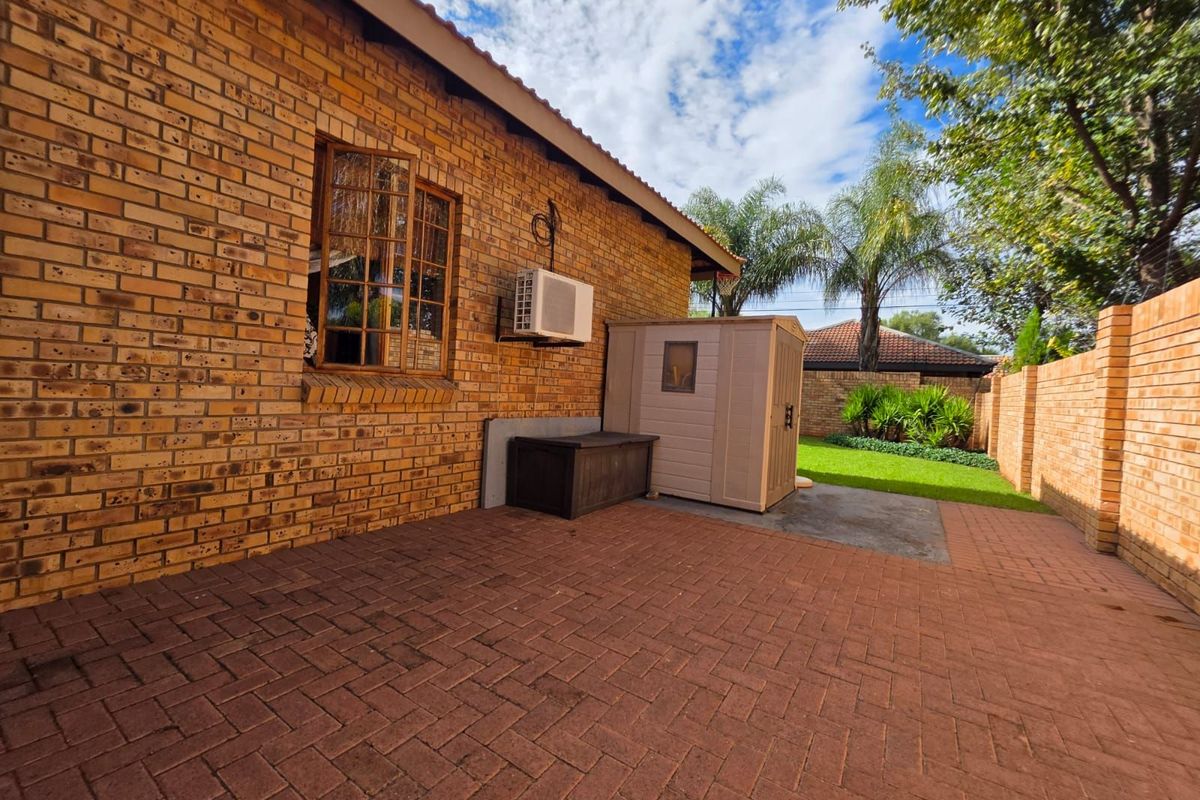 A private rear garden featuring a paved patio area, brick exterior walls, and a small lawn with perimeter brick walling.