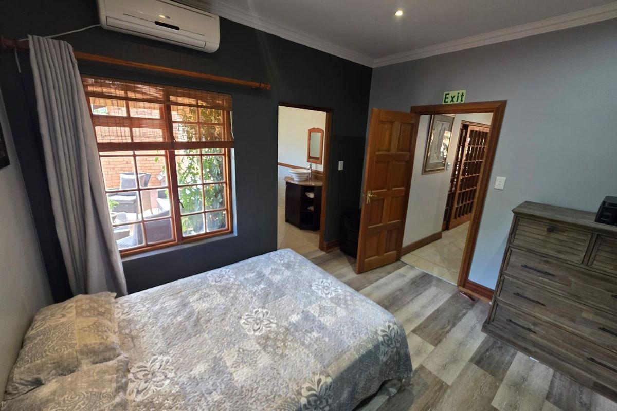 A well-maintained bedroom featuring wood-look flooring, a wall-mounted air conditioning unit, and an en-suite bathroom access.