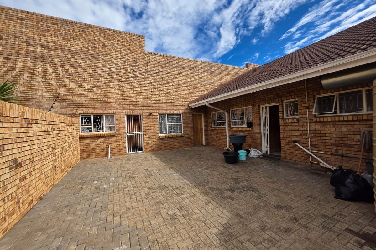 A paved rear courtyard area featuring face-brick walls, security gates, and multiple access points to the main dwelling.