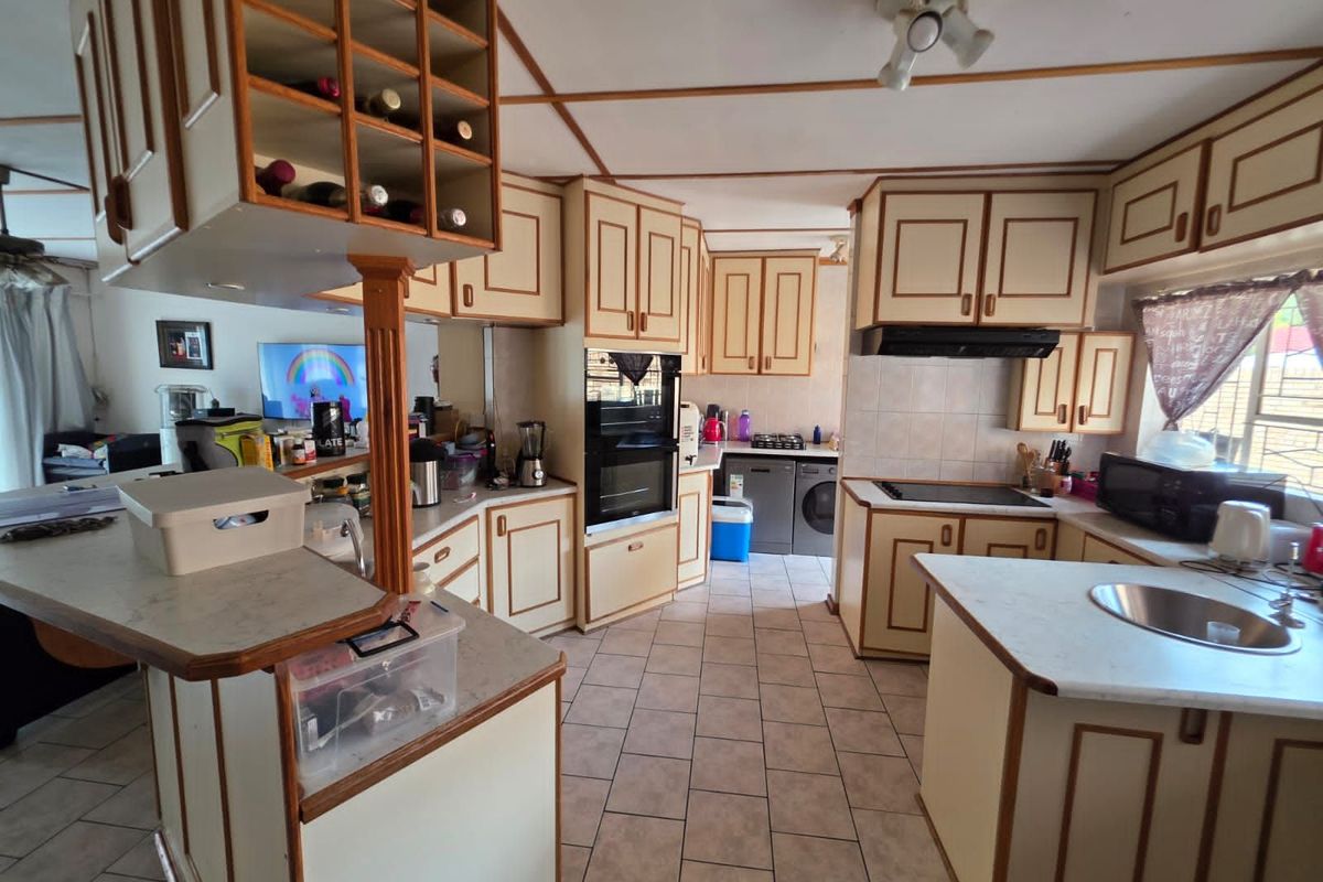 A spacious kitchen featuring built-in cabinetry, integrated oven, hob, extractor fan, and a central island with a stainless steel sink.