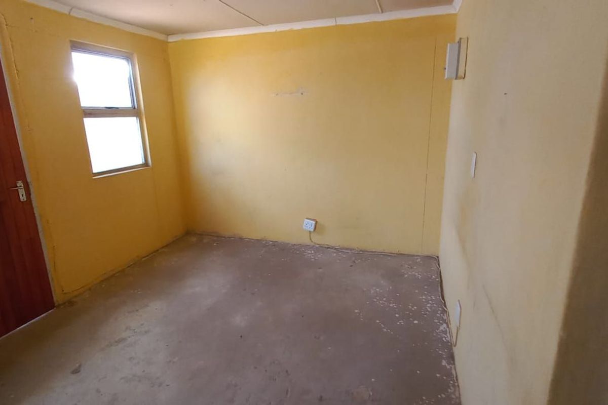 A vacant bedroom featuring yellow painted walls, a wooden door, and unfinished concrete flooring, offering a blank canvas for renovation.