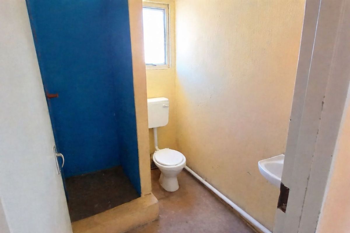 A compact bathroom featuring a toilet, a small wall-mounted basin, and a separate shower enclosure with a blue accent wall.