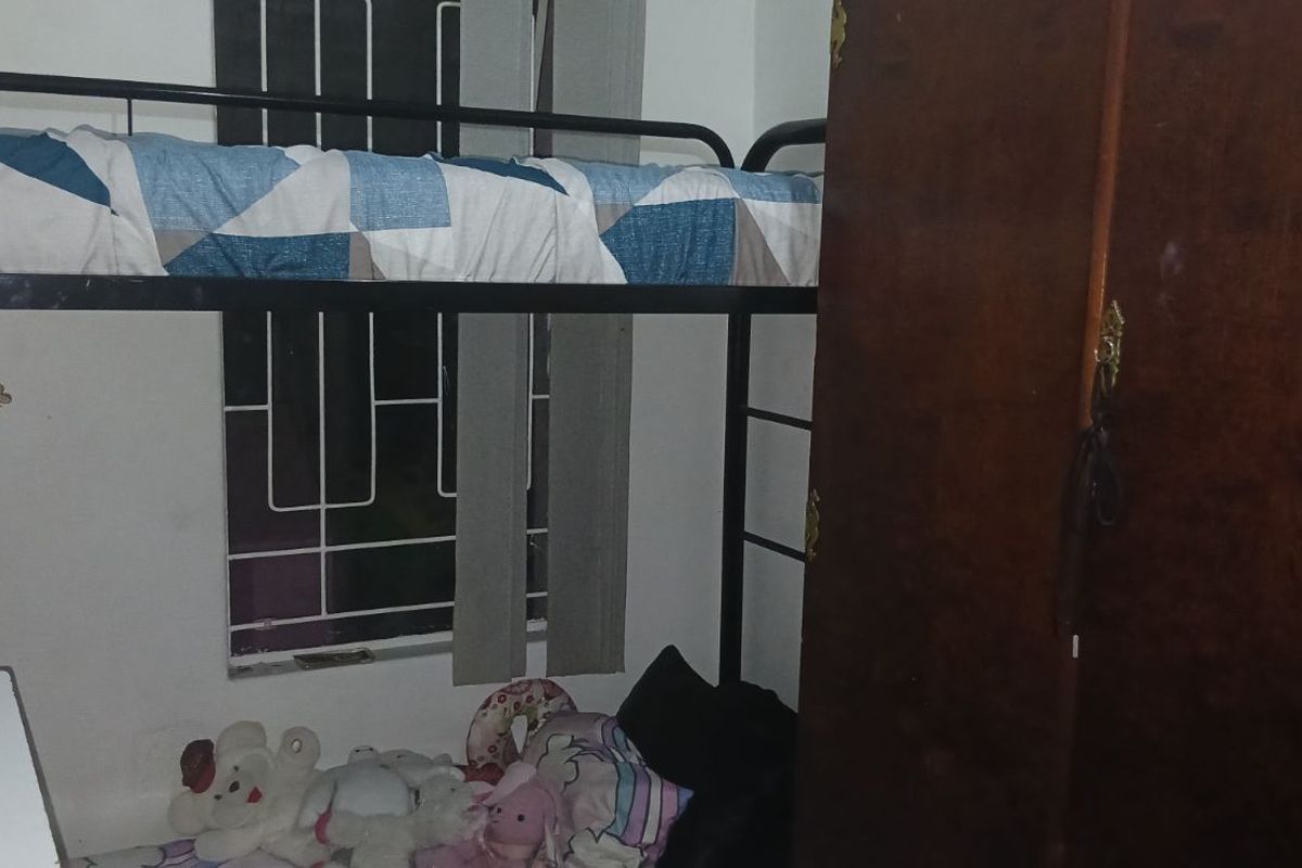A compact bedroom featuring a metal bunk bed frame and a built-in wardrobe, with security bars installed on the window.
