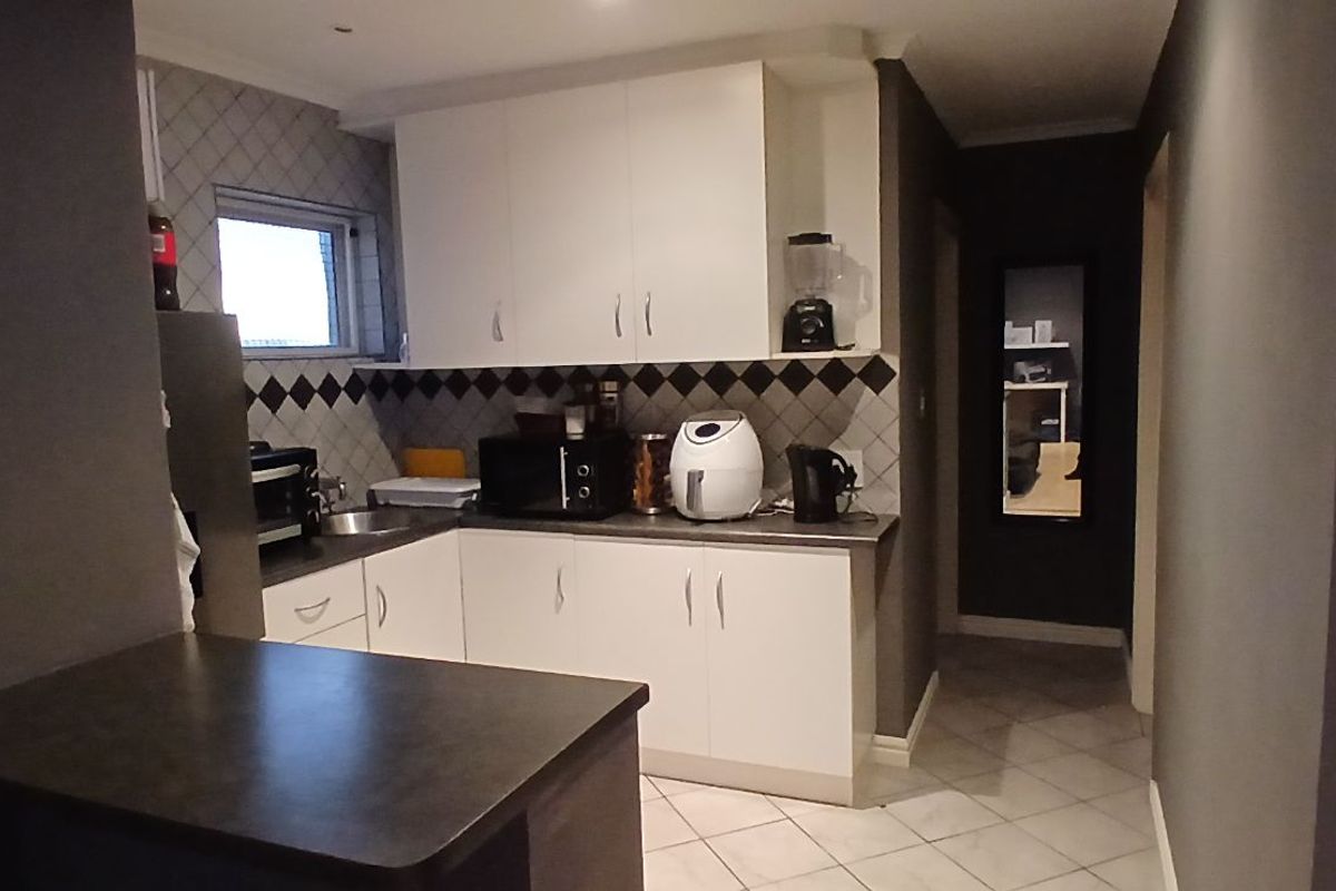 A functional kitchen featuring white cabinetry, dark countertops, and a diamond-patterned tiled backsplash, complemented by neutral floor tiles.