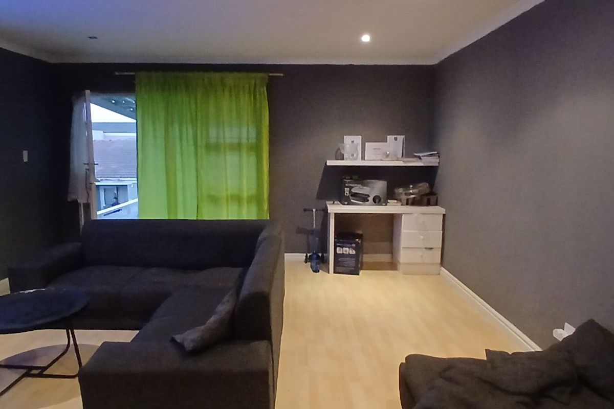 A spacious living room featuring light-toned laminate flooring, dark-painted walls, and a glass door providing access to an outdoor area.