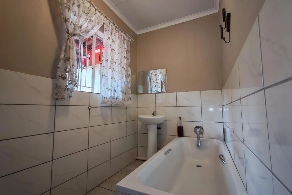 A functional bathroom featuring a white bathtub, pedestal basin, and half-tiled walls with marble-effect ceramic tiles.