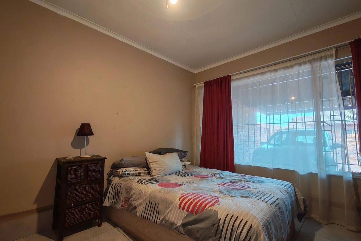 A functional bedroom featuring tiled flooring, a large window with security bars, and neutral wall tones, providing a comfortable living space.