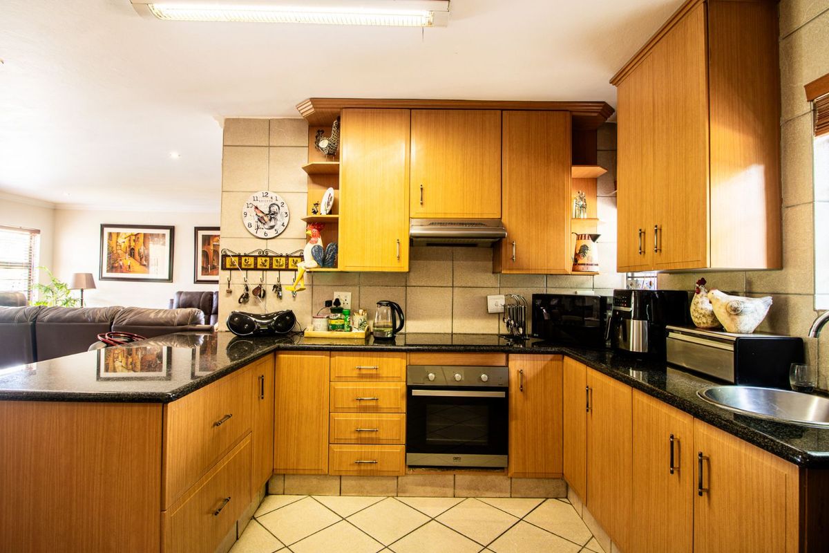 A functional U-shaped kitchen featuring wood-veneer cabinetry, dark granite countertops, built-in oven, extractor fan, and tiled flooring, seamlessly flowing into the adjacent living area.