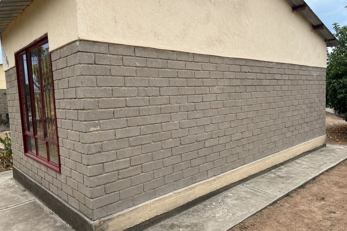 Exterior view of the property showing a brick and plaster facade with a metal-framed window and a concrete perimeter path.