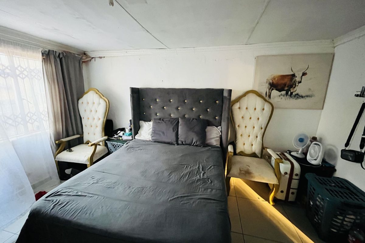 A bedroom featuring tiled flooring and a window with security bars, requiring cosmetic updates to the walls and ceiling.