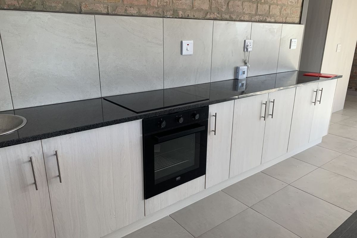 Modern kitchen featuring light wood-grain cabinetry, black granite countertops, integrated oven and hob, and a contemporary tiled backsplash.