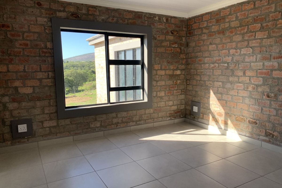 An empty bedroom featuring exposed brick walls, tiled flooring, and a large window with views of the surrounding landscape.