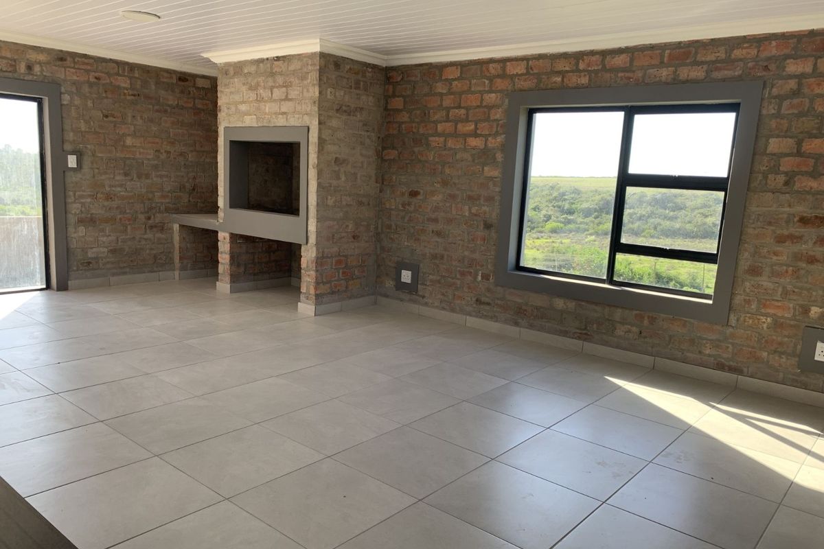 Spacious living area featuring exposed brick walls, tiled flooring, a built-in fireplace, and large windows offering scenic views.