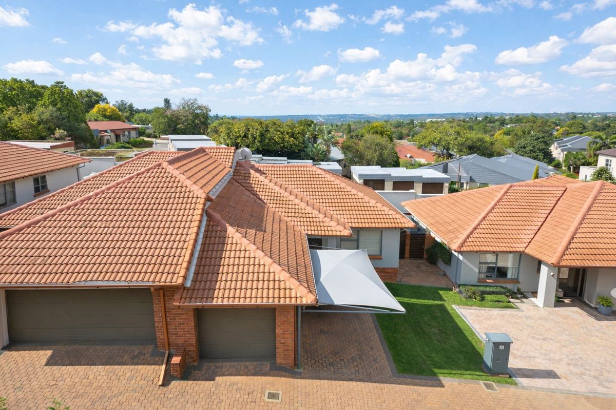 Aerial view of a townhouse complex featuring terracotta tiled roofs, paved driveways, double garages, and a small private garden area with a shade sail.