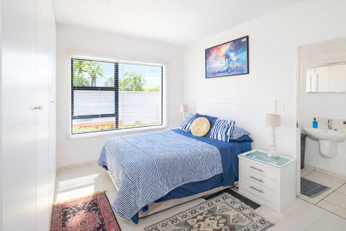 A bright bedroom featuring built-in wardrobes, tiled flooring, and an en-suite bathroom with a wall-mounted basin.