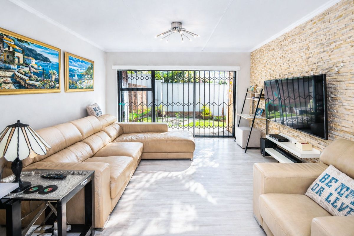 A bright living room featuring a textured stone feature wall, light wood-look flooring, and sliding glass doors with security gates leading to the garden.