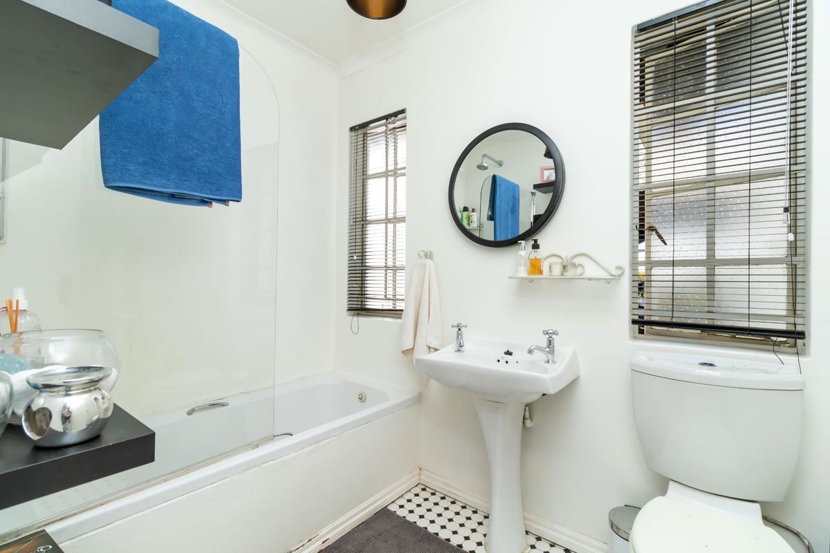 A functional bathroom featuring a pedestal basin, a bathtub with a glass shower screen, and classic black and white mosaic floor tiles.